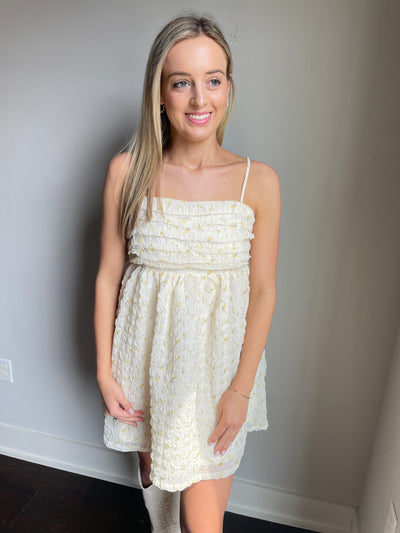 The Ivy Babydoll Dress from Shop Silvs is a cream-colored babydoll dress with a ruffled bodice and spaghetti straps. 