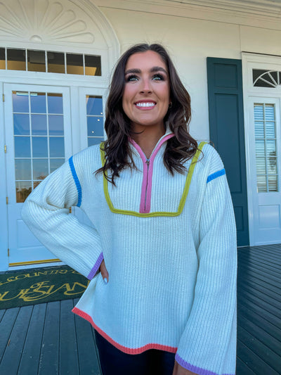 The Happy Days Half Zip from Shop Silvs is a white half zip sweater with bell sleeves and colorful stitch detailing.