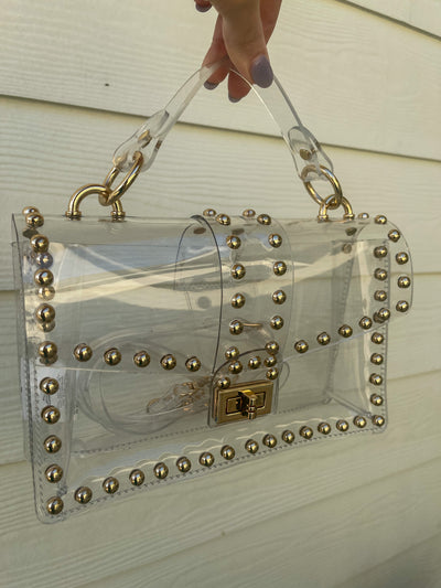 This Gold Round Studded Clear Bag is a see-through bag with gold studs, ideal for game day at the stadium.